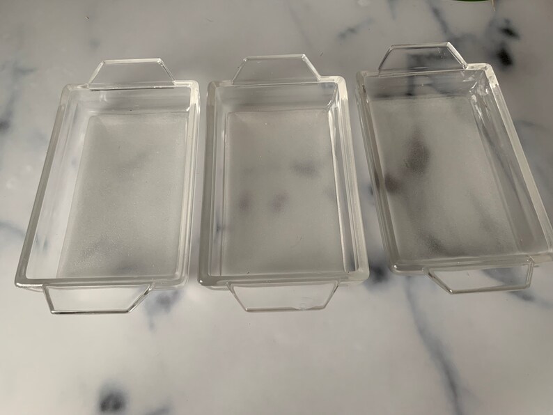K&ouml;nnte beinhalten: Drei transparente Glasbackformen mit Griffen. Die Formen sind rechteckig und haben eine matte Oberfl&auml;che.