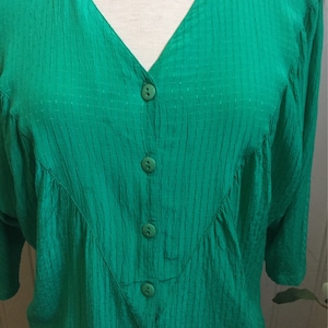Puede incluir: Una blusa verde con botones, cuello en V y tejido texturizado.