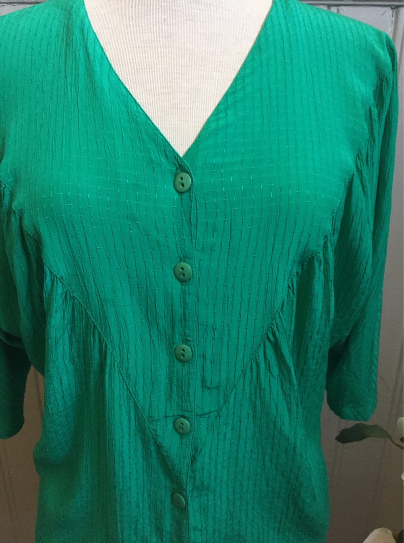 Puede incluir: Una blusa verde con botones, cuello en V y tejido texturizado.