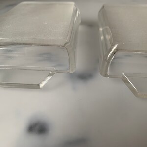 K&ouml;nnte beinhalten: Zwei rechteckige Beh&auml;lter aus klarem Kunststoff mit einem erh&ouml;hten Rand oben und einem Rand unten. Die Beh&auml;lter sind leer und scheinen aus einem strapazierf&auml;higen Material zu bestehen.