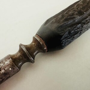 May include: Close-up of a vintage knife. The handle is dark brown and textured, leading to a black section near the blade. The blade's base is a rusty, aged metal. The knife has a decorative, ornate design.