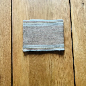 May include: A folded fabric napkin with a brown and white striped pattern. The napkin has a subtle sheen and a slightly textured surface.