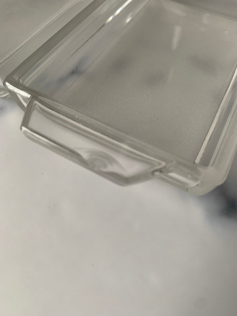K&ouml;nnte beinhalten: Eine rechteckige Glasschale aus klarem Glas mit erh&ouml;htem Rand und einem Griff an einer Seite. Die Schale ist leer und scheint aus mattiertem Glas zu sein.