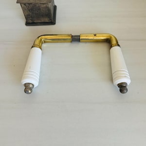 May include: A brass door handle with white porcelain knobs. The handle is in two pieces, with a brass connecting piece in the middle.