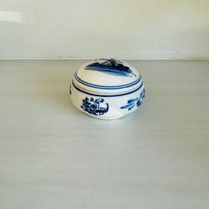 May include: A white ceramic trinket box with a blue and white windmill design. The box is round and has a lid.