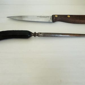 May include: Two kitchen tools: a Butcher Block Knives brand knife with a wooden handle and a steel blade, and a sharpening steel with a black handle. The knife has a dark brown handle with brass rivets.