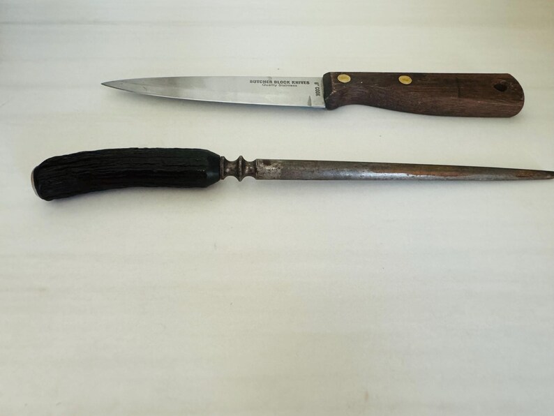May include: Two kitchen tools: a Butcher Block Knives brand knife with a wooden handle and a steel blade, and a sharpening steel with a black handle. The knife has a dark brown handle with brass rivets.