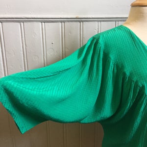 Puede incluir: Una blusa verde de seda con cuello en V y mangas abullonadas.