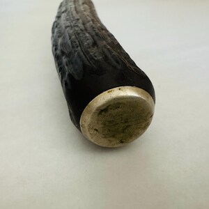 May include: Close-up of a decorative bottle stopper. The stopper features a dark, textured body with a silver-coloured metal base. The body has a dark, almost black colour, with lighter grey and brown tones.