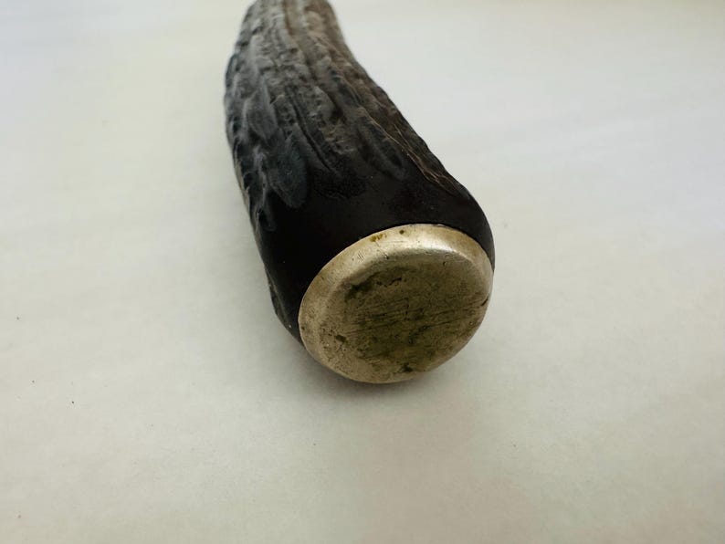 May include: Close-up of a decorative bottle stopper. The stopper features a dark, textured body with a silver-coloured metal base. The body has a dark, almost black colour, with lighter grey and brown tones.