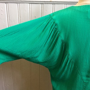 Puede incluir: Una blusa verde de manga larga con un tejido texturizado y arrugado. La blusa tiene un escote en V y un corte holgado.