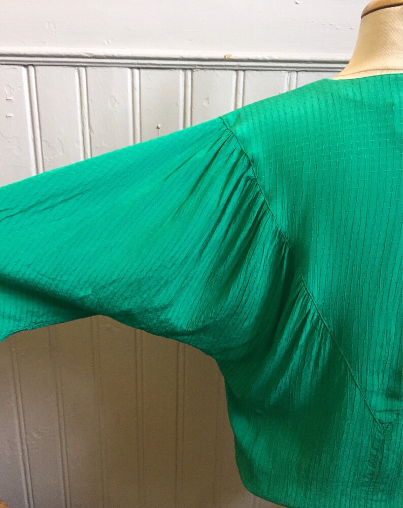 Puede incluir: Una blusa verde de manga larga con un tejido texturizado y arrugado. La blusa tiene un escote en V y un corte holgado.