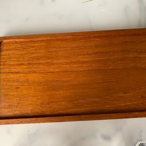 K&ouml;nnte beinhalten: Ein rechteckiges Holztablett mit erh&ouml;htem Rand. Das Tablett ist aus hellbraunem Holz mit glatter Oberfl&auml;che.