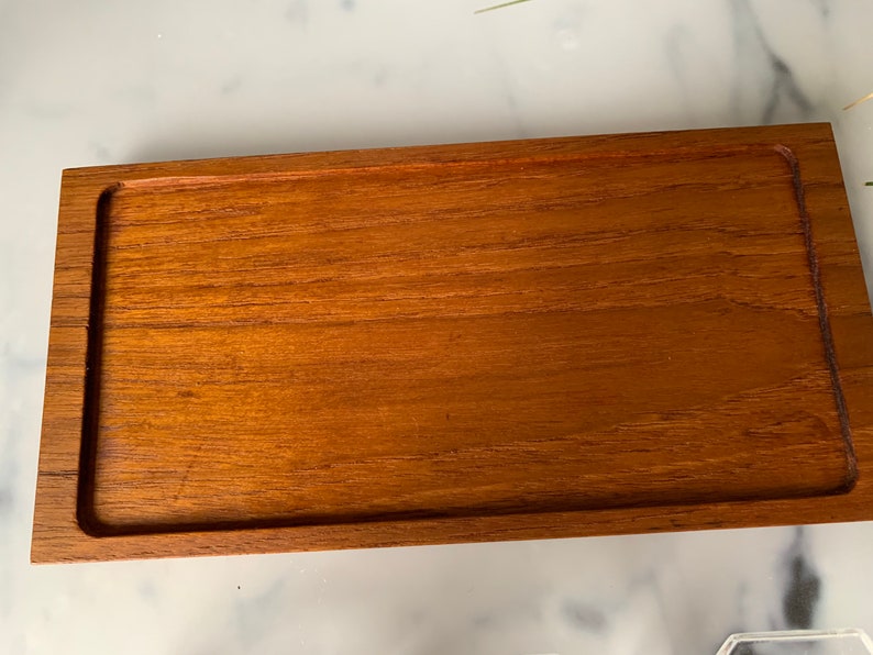 K&ouml;nnte beinhalten: Ein rechteckiges Holztablett mit erh&ouml;htem Rand. Das Tablett ist aus hellbraunem Holz mit glatter Oberfl&auml;che.