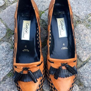 May include: A pair of brown leather loafers with black tassel accents. The shoes have a checkered pattern and are labeled "Gabor International" with the size "4" and "Made in W-Germany".