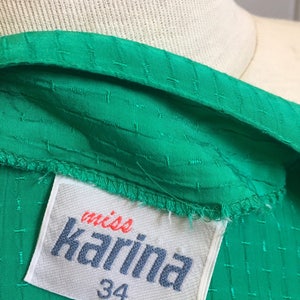Puede incluir: Una tela verde texturizada con una etiqueta blanca que dice "miss Karina" y "34" en letras azules.