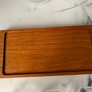 K&ouml;nnte beinhalten: Ein rechteckiges Holztablett mit erh&ouml;htem Rand. Das Tablett ist aus hellbraunem Holz mit glatter Oberfl&auml;che.