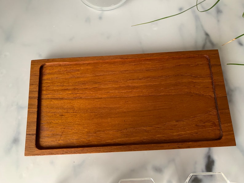 K&ouml;nnte beinhalten: Ein rechteckiges Holztablett mit erh&ouml;htem Rand. Das Tablett ist aus hellbraunem Holz mit glatter Oberfl&auml;che.