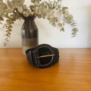 May include: A black braided belt with a large, round, gold-toned buckle.