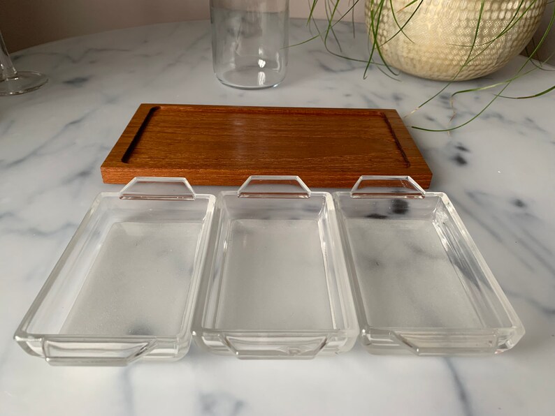 K&ouml;nnte beinhalten: Drei rechteckige Glasschalen mit abgerundeten Kanten und Griffen auf einem Holztablett. Die Schalen sind leer und bereit, mit Snacks oder Vorspeisen gef&uuml;llt zu werden.