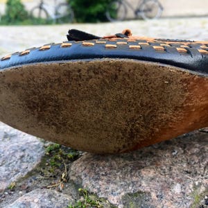 May include: The bottom of a brown leather shoe with a black woven leather upper. The shoe has a worn leather sole.
