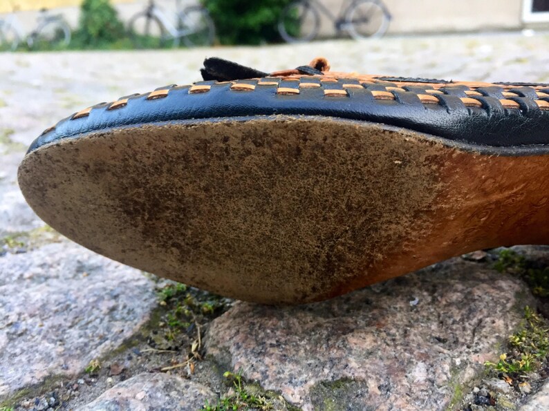 May include: The bottom of a brown leather shoe with a black woven leather upper. The shoe has a worn leather sole.