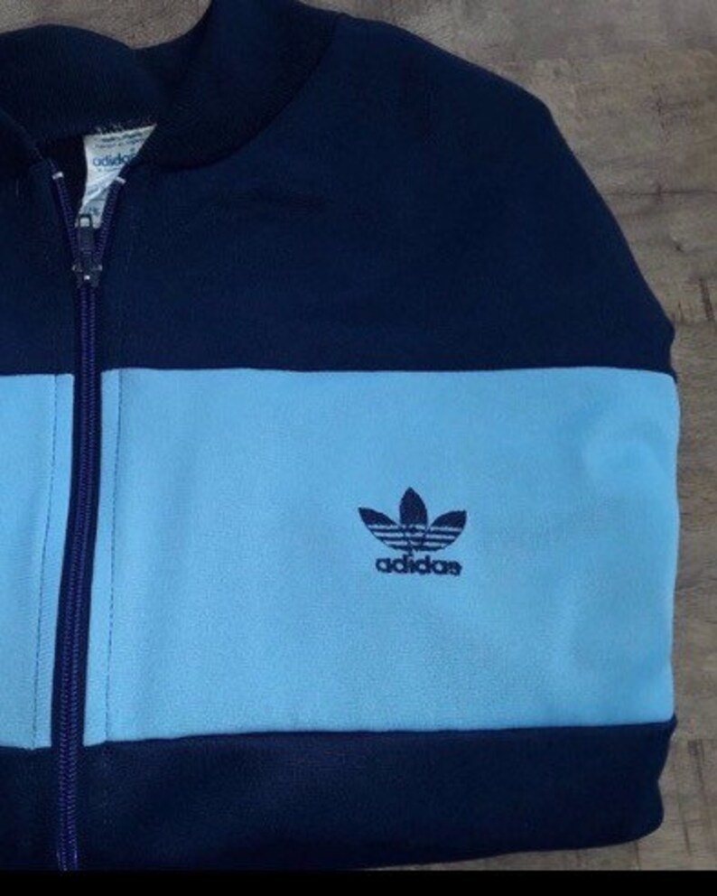 May include: A blue and light blue Adidas zip-up jacket with the Adidas logo on the front.