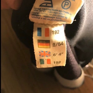 May include: A white tag with a black border and blue, red, and yellow flags. The tag has the numbers 192, 8/54, and 6'4" printed on it. The tag also has the number 192 printed on it.