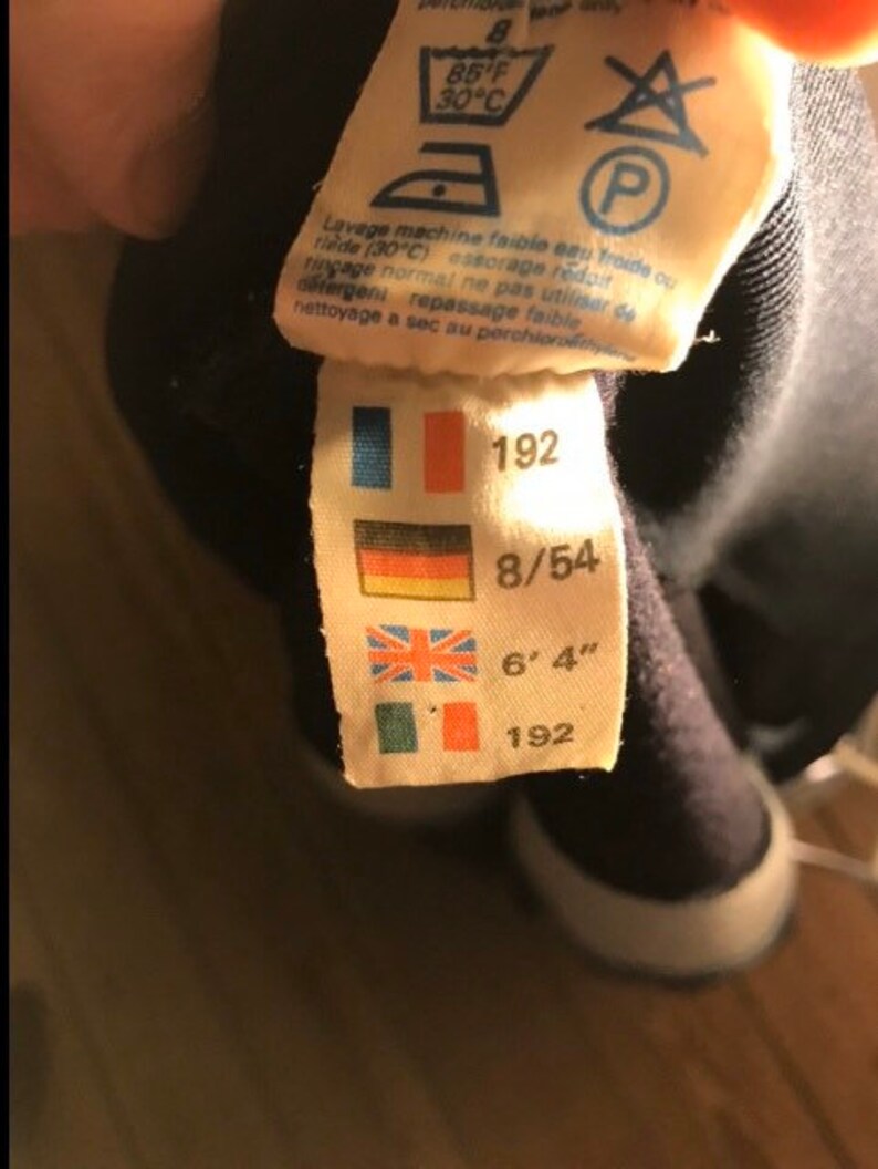 May include: A white tag with a black border and blue, red, and yellow flags. The tag has the numbers 192, 8/54, and 6'4" printed on it. The tag also has the number 192 printed on it.