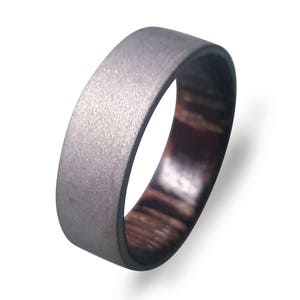 May include: A silver and brown ring with a textured finish. The ring is made of titanium and wood.