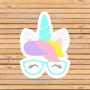 May include: A sticker of a unicorn with a blue horn, pink and yellow mane, and purple and pink ears. The unicorn is wearing blue glasses with eyelashes.