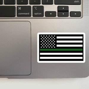 May include: A black and white American flag with a green stripe across the middle. The flag is on a silver laptop.
