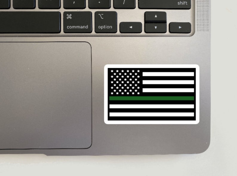 May include: A black and white American flag with a green stripe across the middle. The flag is on a silver laptop.