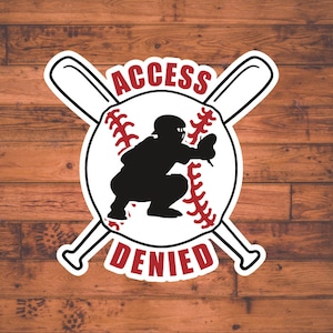 May include: A white baseball with red stitching and a black silhouette of a baseball catcher in a crouching position. The baseball is surrounded by two crossed baseball bats. The text "ACCESS DENIED" is written in red and white letters above and below the baseball.