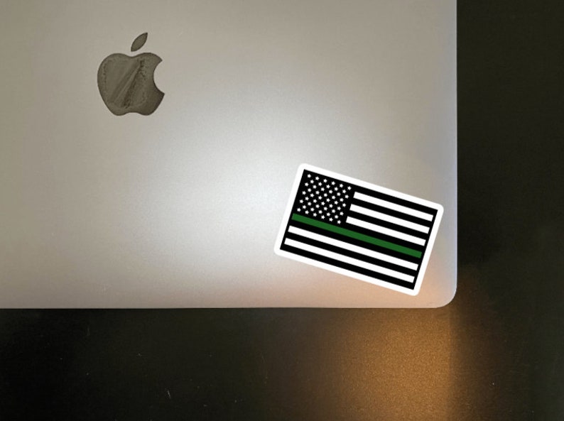 May include: A black and white American flag sticker with a green stripe across the middle. The sticker is on a silver laptop.