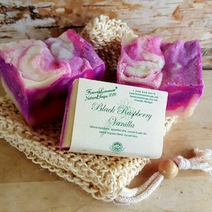 May include: Three bars of handmade soap with a swirl of pink, purple, and white colors, resting on a beige sisal soap saver. A label reads "Black Raspberry Vanilla" with the brand name "Forever Summer Natural Soaps LLC".
