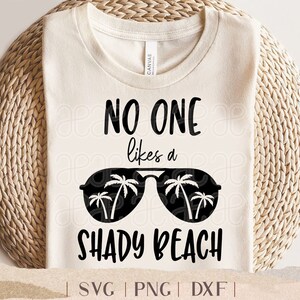 May include: A white t-shirt with the text "NO ONE likes a SHADY BEACH" in black lettering. The text is surrounded by a pair of sunglasses with palm trees inside the lenses.