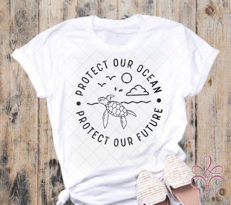 May include: White t-shirt featuring a black graphic of a sea turtle swimming in the ocean, with the text "PROTECT OUR OCEAN PROTECT OUR FUTURE" in a circular design. The shirt is made of a soft material.