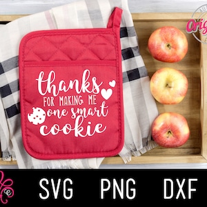 May include: Red quilted pot holder with the text "thanks for making me one smart cookie" in white. The pot holder is on a black and white checkered fabric with three red apples in a wooden tray.