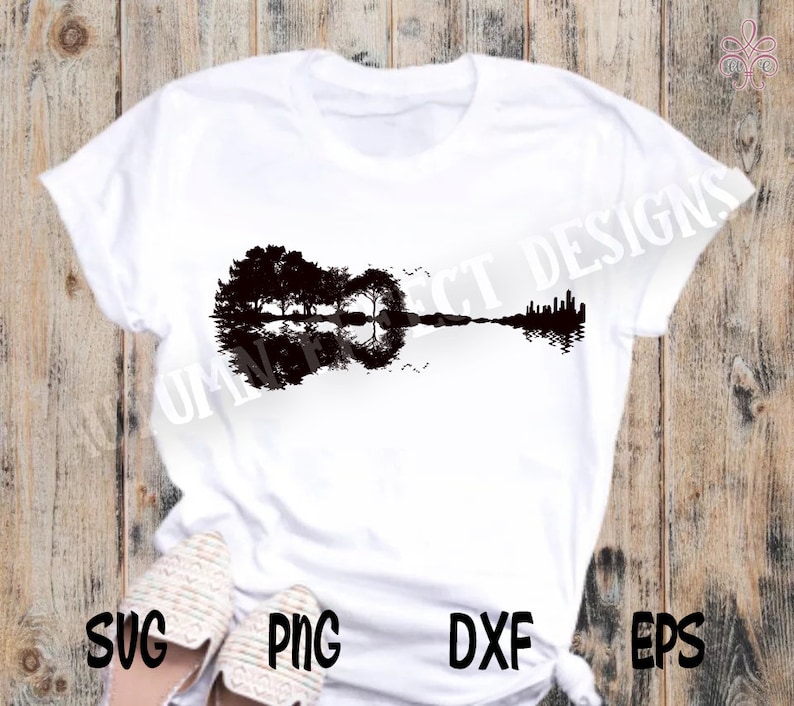 May include: A white t-shirt featuring a black silhouette of a guitar with trees reflected in the water. The guitar is formed by the reflection of the trees in the water.