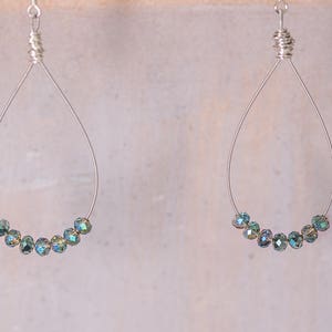 May include: A pair of silver teardrop earrings. Each earring has a wire frame with a cluster of iridescent, teal-coloured beads at the base. The beads have a shimmering, multi-tonal effect, adding a touch of elegance to the design.