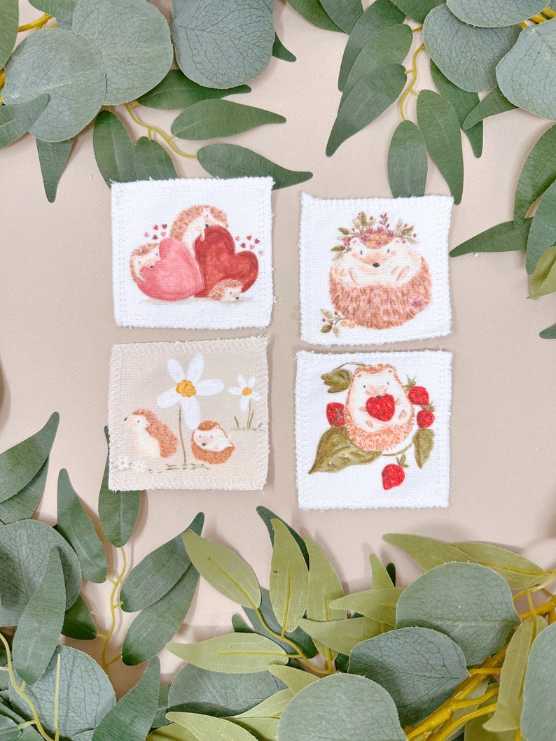 Puede incluir: Cuatro cuadrados de tela blanca con diferentes dise&ntilde;os de erizos. El primer cuadrado muestra una familia de erizos con un coraz&oacute;n rojo. El segundo cuadrado muestra un erizo con una corona de flores. El tercer cuadrado muestra un erizo con una margarita. El cuarto cuadrado muestra un erizo con fresas.