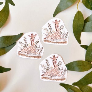 May include: Three stickers featuring a cute cartoon giraffe sitting in a patch of green grass. The giraffe is brown with white spots and has a long neck and long legs. The stickers are perfect for adding a touch of whimsy to your planner, laptop, or water bottle.