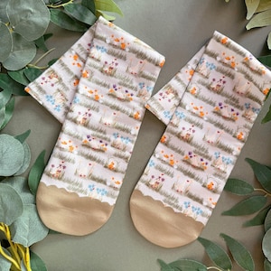 May include: A pair of white socks with a beige trim. The socks feature a repeating pattern of small orange and white birds, blue flowers, and green grass.