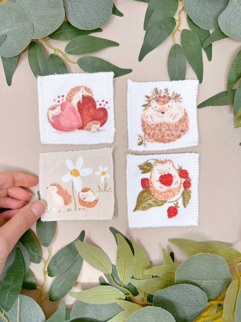 Puede incluir: Cuatro cuadrados de tela blanca con im&aacute;genes bordadas de erizos. Un cuadrado presenta un erizo con una corona de flores, otro tiene un erizo con corazones, otro tiene un erizo con fresas y el &uacute;ltimo tiene un erizo con margaritas.