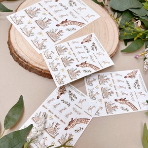 Może przedstawiać: Trzy arkusze papieru z naklejkami z żyrafami na białym tle, z ż&oacute;łtymi kwiatami i zielonymi liśćmi. Tekst na arkuszu naklejek brzmi "Giraffe Sticker Sheet".
