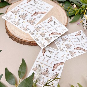 Może przedstawiać: Trzy arkusze papieru z naklejkami z żyrafami z ilustracjami żyraf w dżungli. Naklejki są na białym papierze z nadrukiem "Giraffe Sticker Sheet" na każdym arkuszu.