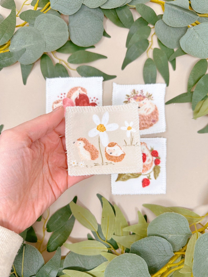 Puede incluir: Cuatro cuadrados de tela bordados con un dise&ntilde;o de erizo. Un cuadrado muestra un erizo con una corona de flores, otro muestra un erizo con un coraz&oacute;n, otro muestra un erizo con una flor y el &uacute;ltimo muestra un erizo con fresas.