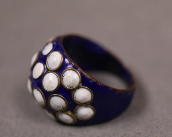 Puede incluir: Un anillo azul con puntos de esmalte blanco. El anillo es de metal y tiene una forma redondeada.