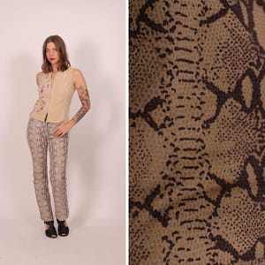 May include: A beige vest with floral embroidery and matching snake print trousers. The trousers have a light brown and dark brown pattern. The outfit is paired with black shoes. The image also shows a close-up of the snake print fabric.